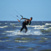Aula de kitesurf para iniciantes com instrutor e equipamento completo em praia de Florianópolis com vento constante.