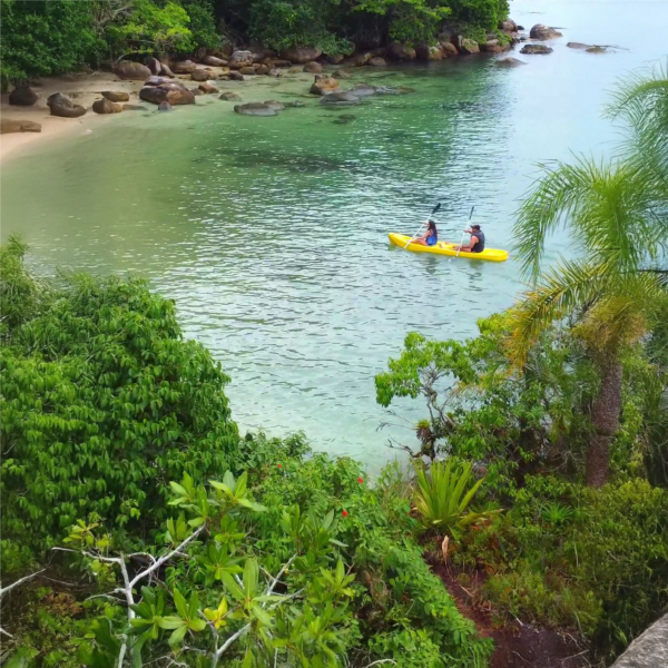 Casal remando até a Ilha do Francês em caiaque durante passeio romântico com parada para relax e fotos.
