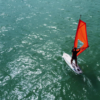 Aluno praticando windsurf na água com vento favorável e orientação de instrutor em Florianópolis.