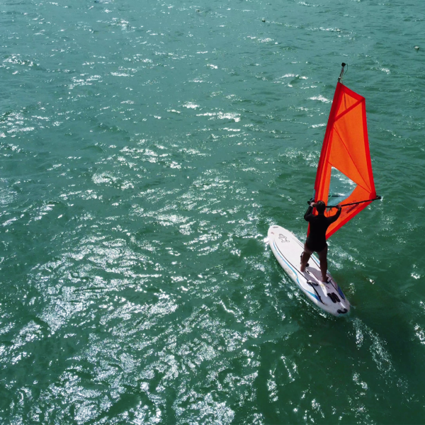 Aluno praticando windsurf na água com vento favorável e orientação de instrutor em Florianópolis.